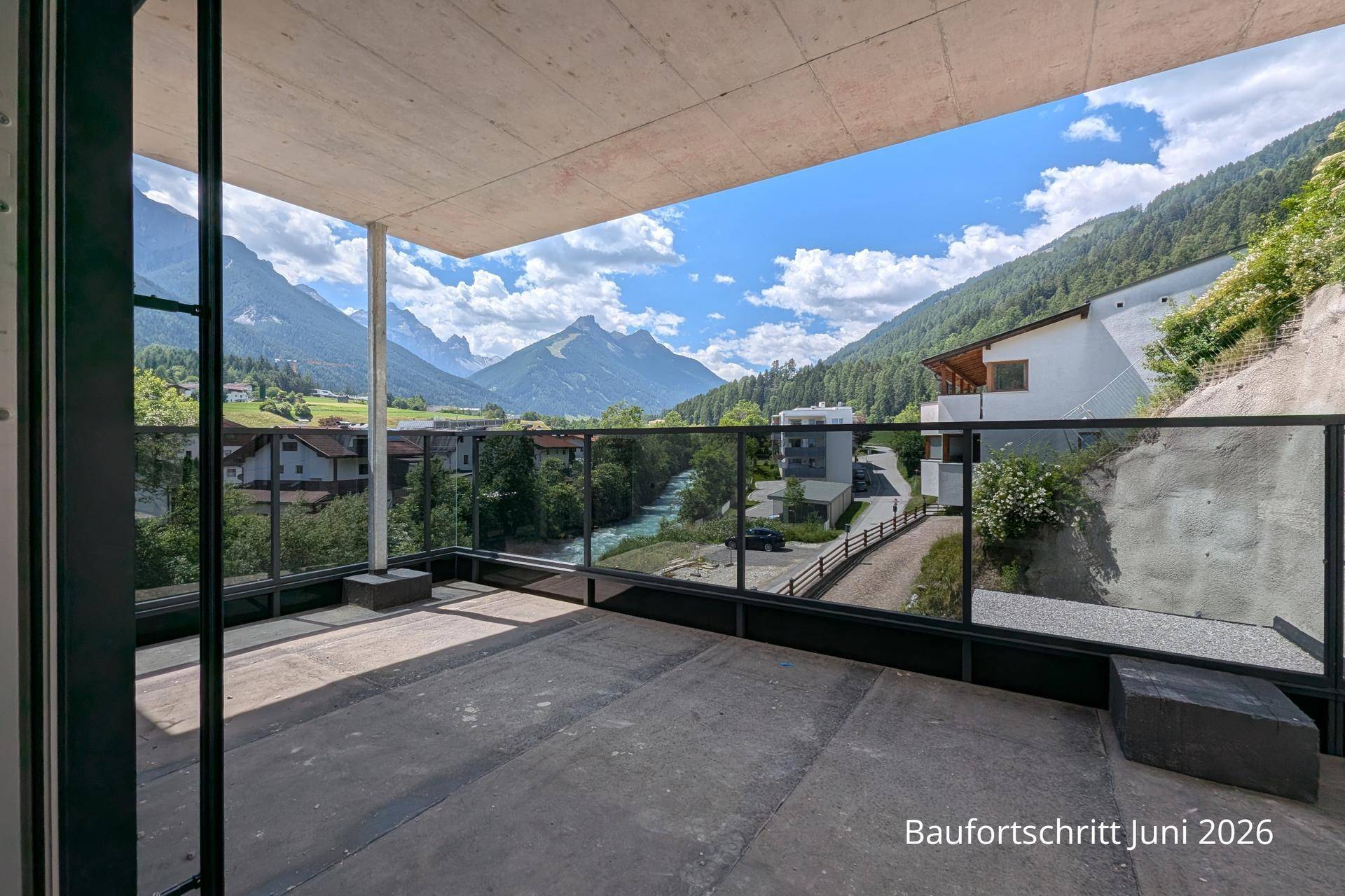 Heller Balkon mit moderner Glasbrüstung und weitem Blick über das Tal und die Berge.
