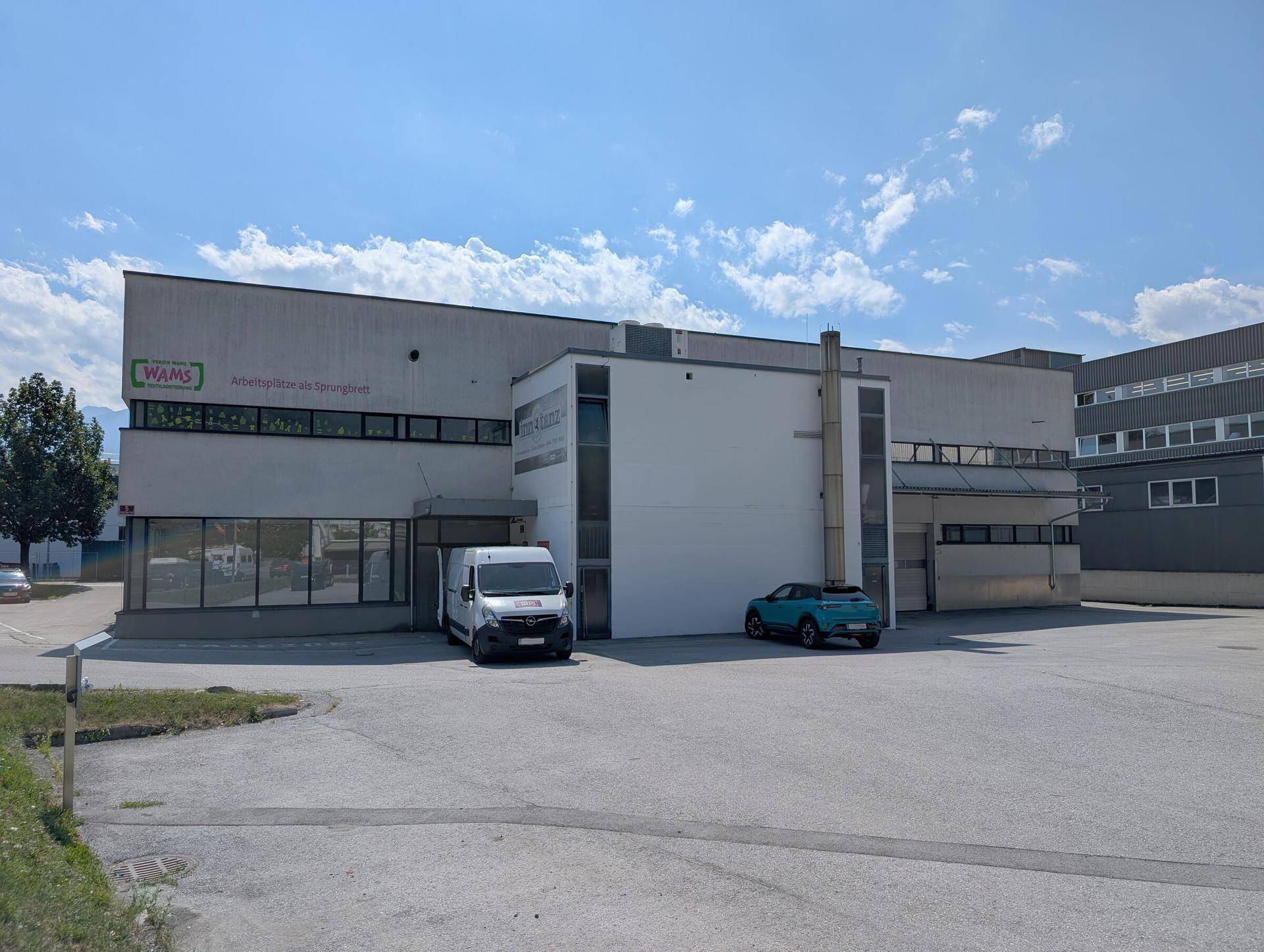 Gebäudeansicht eines modernen Gewerbeobjekts mit großem Parkplatz unter blauem Himmel.