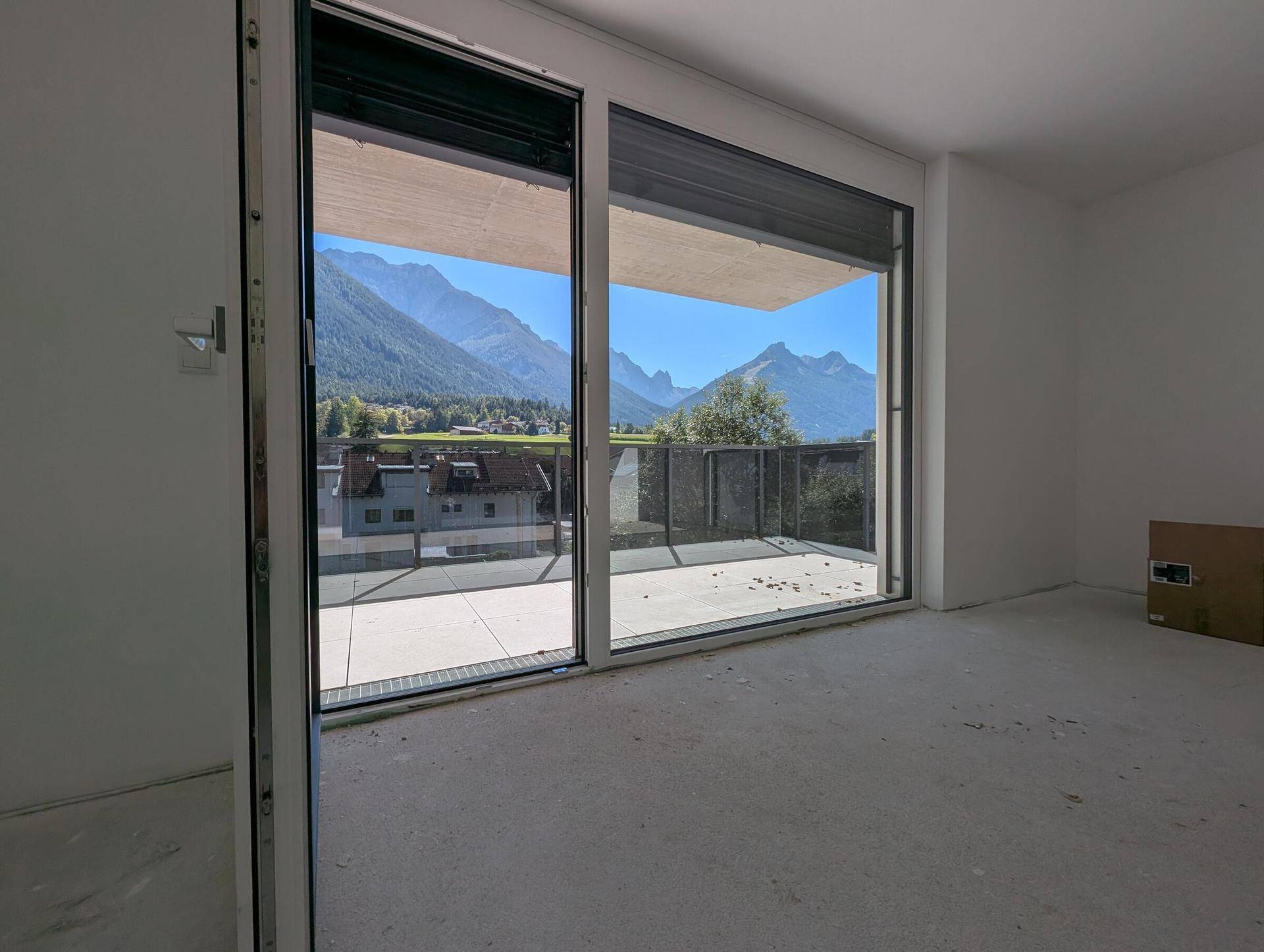 Heller, unmöblierter Raum mit großen Fenstern und direktem Zugang zum Balkon mit Bergblick.