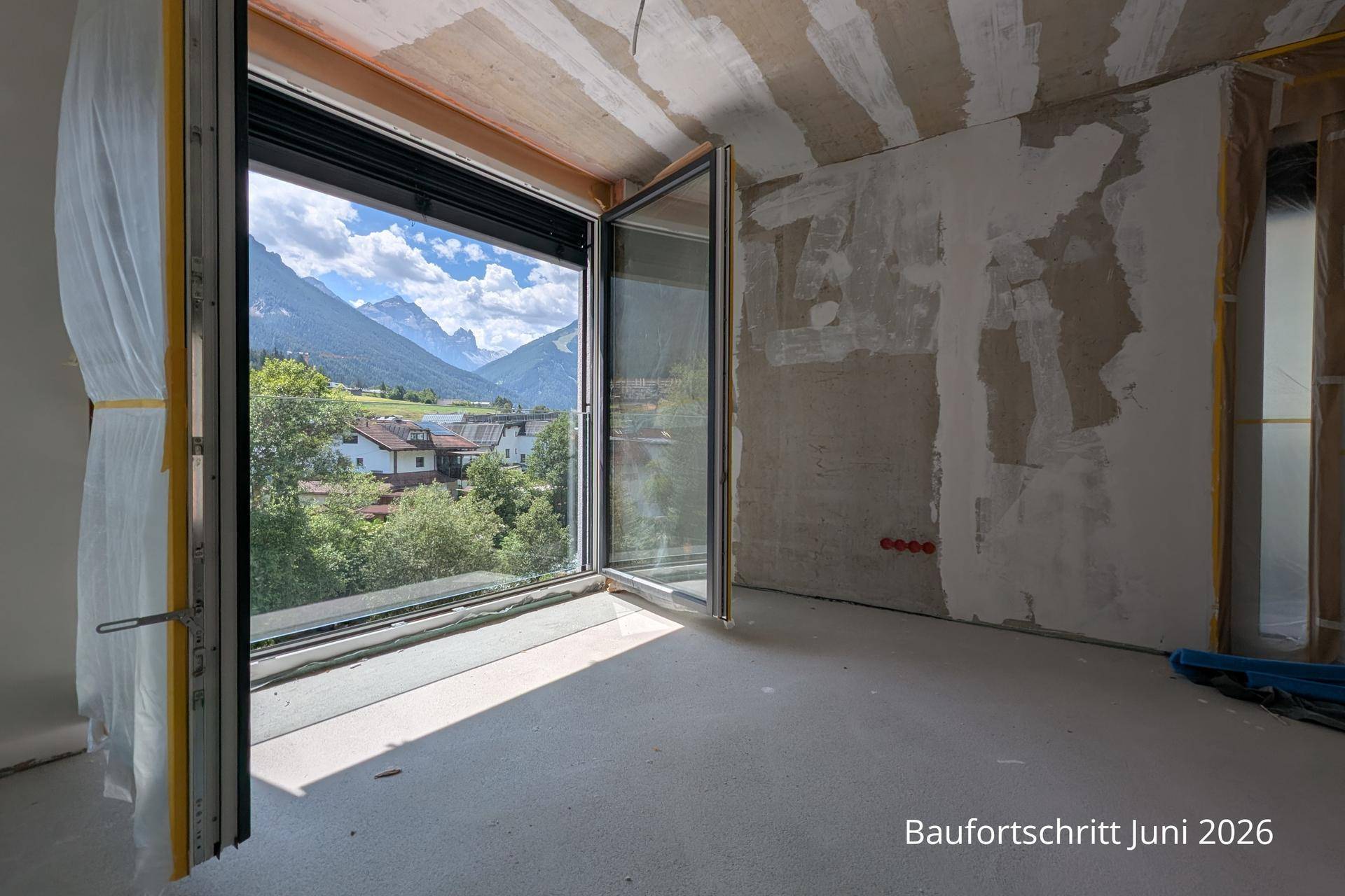 Unfertiger Innenraum mit großen Fenstern, die einen weiten Blick auf die Berge bieten.