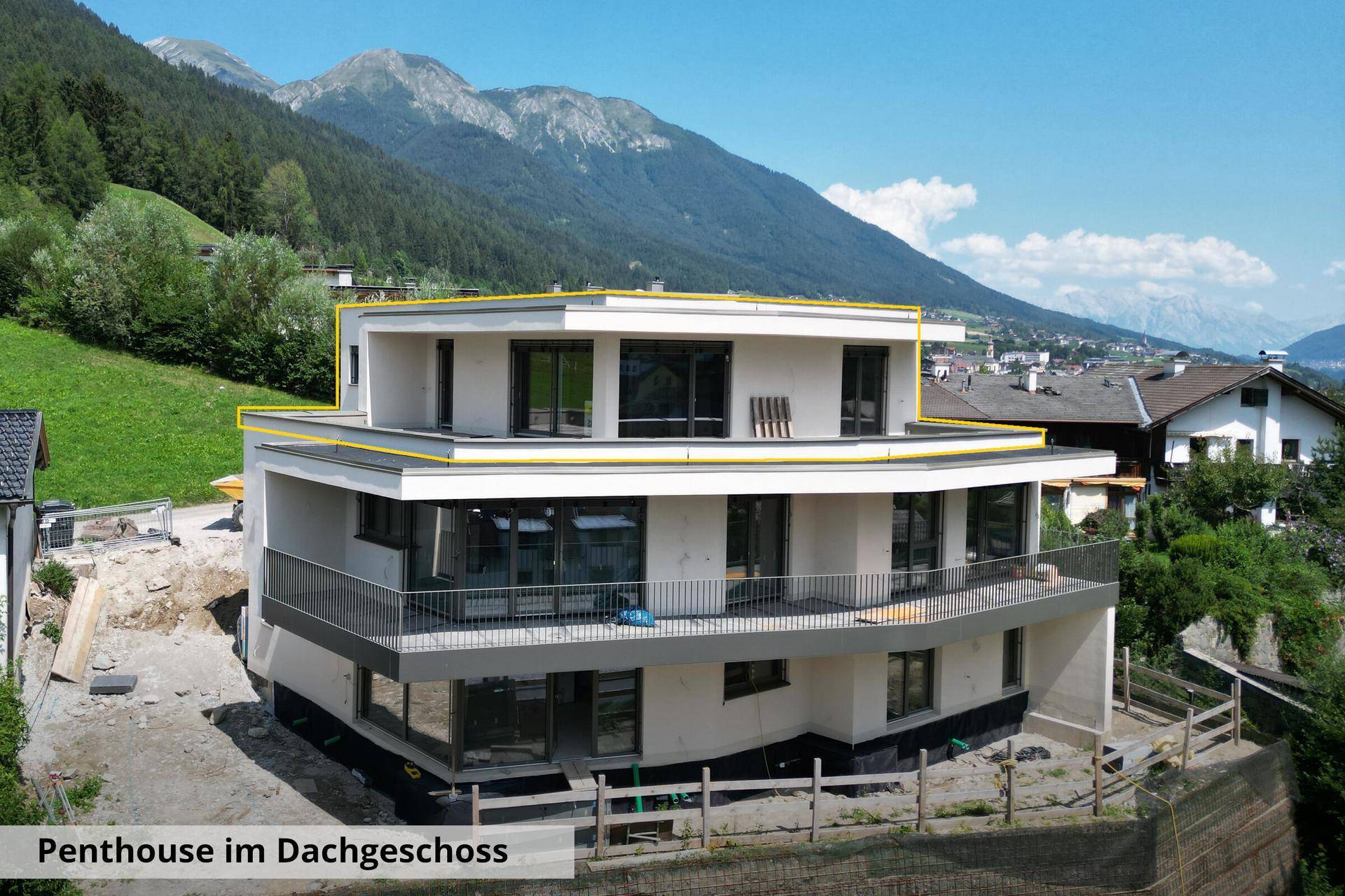 Nahaufnahme eines modernen Neubaus mit Flachdach und großen Balkonen, umgeben von einer alpinen Landschaft.