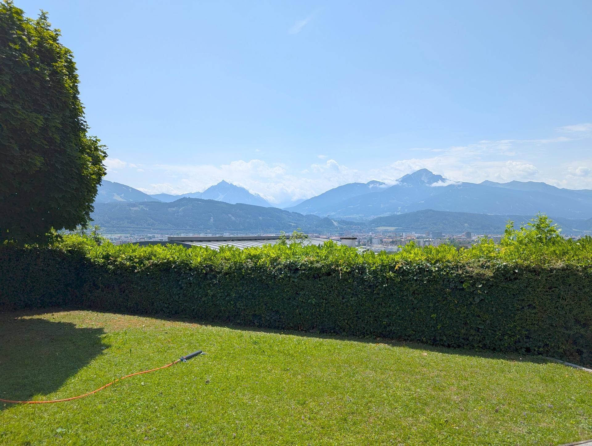 Weitläufiger Gartenbereich mit grüner Hecke und einem atemberaubenden Panoramablick auf die umliegende Berglandschaft.