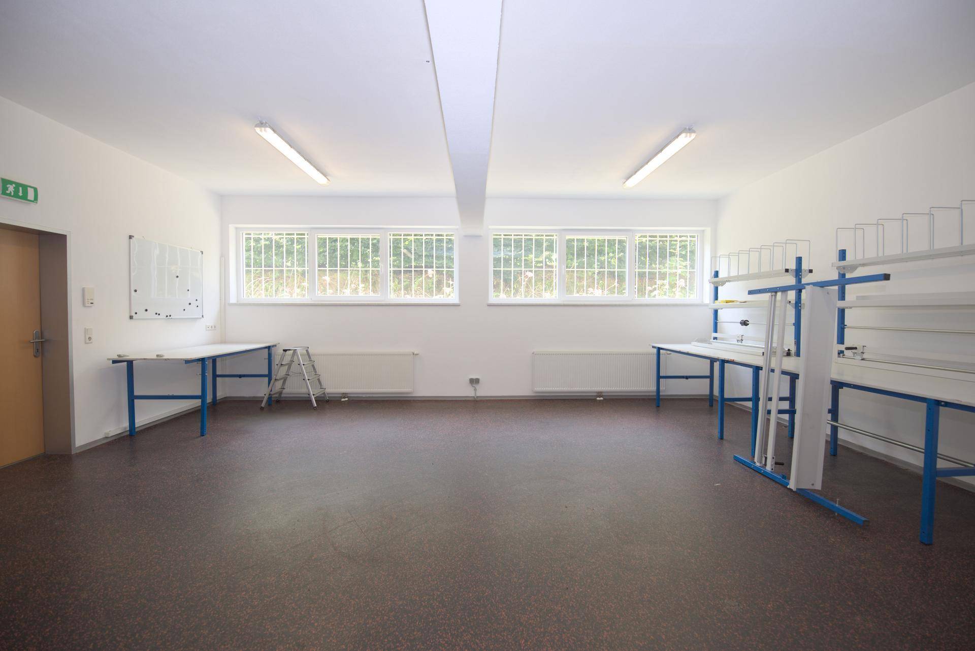 Heller Arbeitsraum mit großen Fenstern, robusten Arbeitstischen und Regalen, ideal für Werkstatt oder Büro.