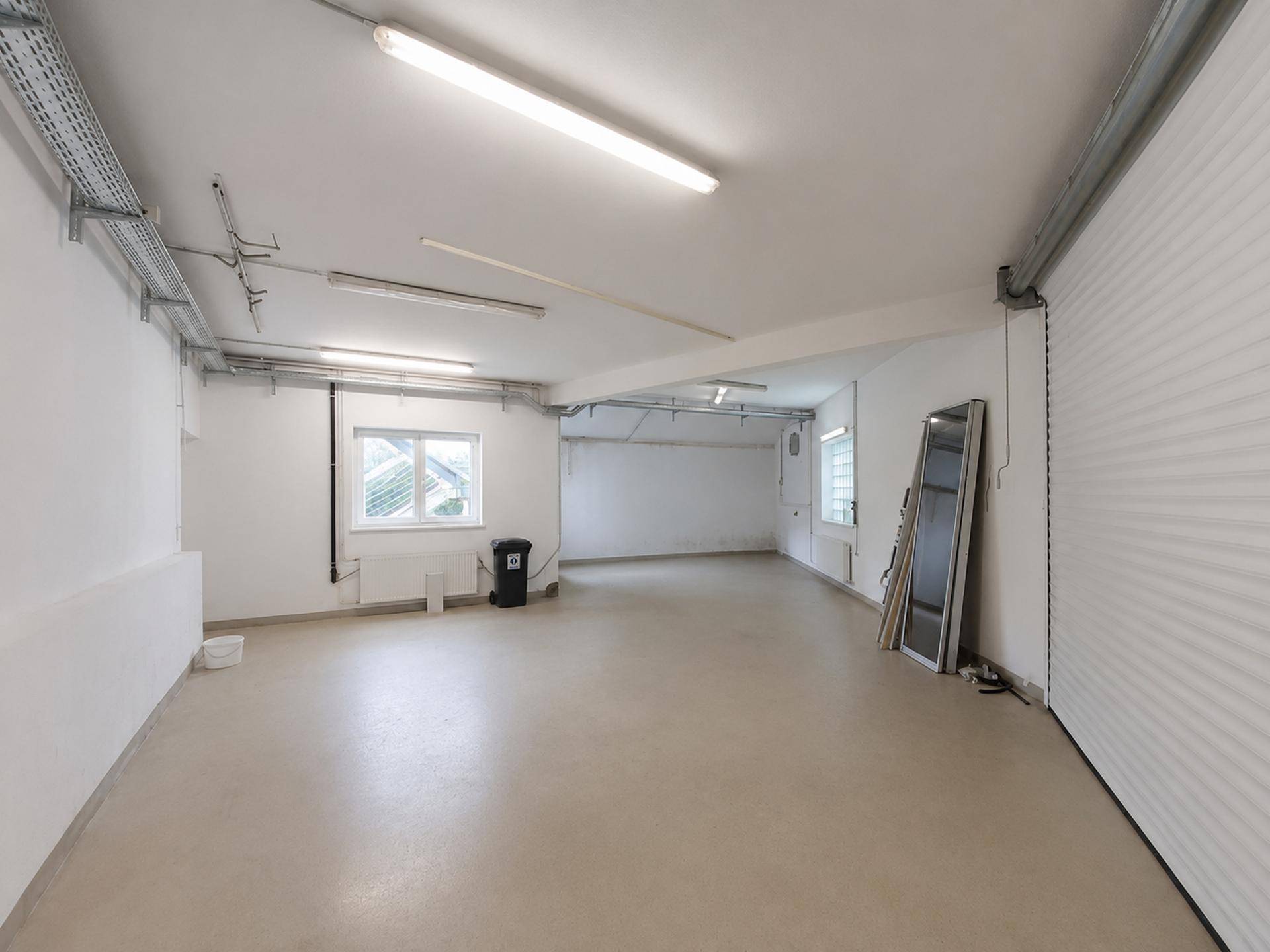 Geräumiger, leerer Gewerberaum mit Betonboden, Fenstern und industrieller Beleuchtung an der Decke.