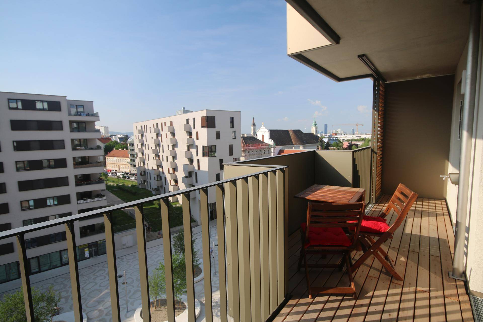 Balkon mit Holzboden und Sitzgelegenheiten, bietet Blick auf die Stadt und umliegende Gebäude.