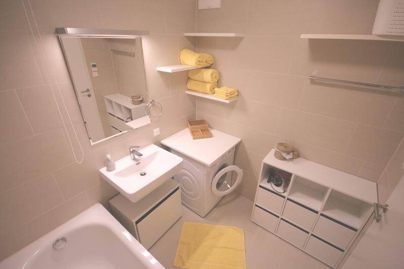 Modernes Badezimmer mit Badewanne, Waschbecken und Waschmaschine in hellen Fliesen.