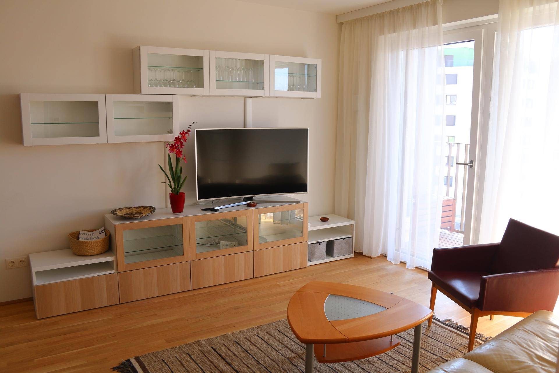 Heller Wohnbereich mit TV-Möbeln, großen Fenstern und Zugang zum Balkon.