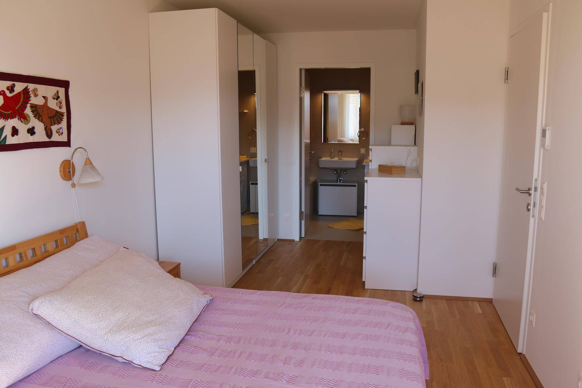 Schlafzimmer mit Holzbett, Spiegelschränken und direktem Zugang zum Badezimmer.
