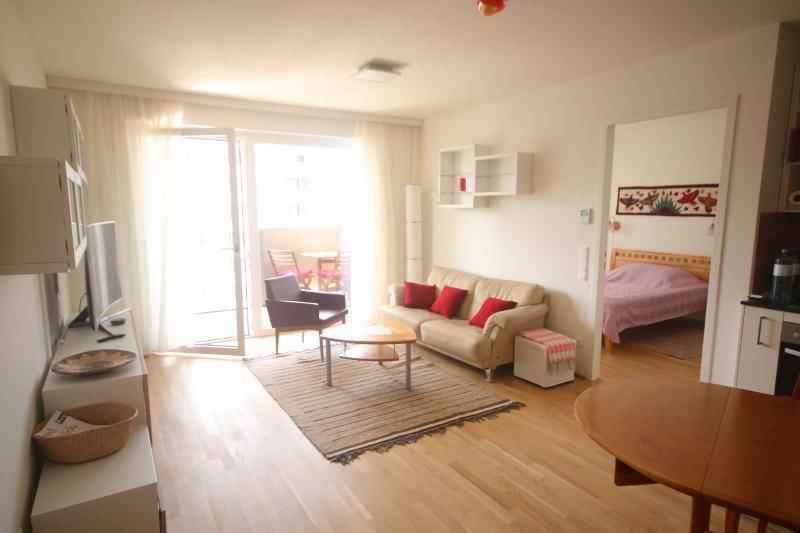 Wohnbereich mit Sofa, Zugang zum Balkon und Blick in ein angrenzendes Schlafzimmer.