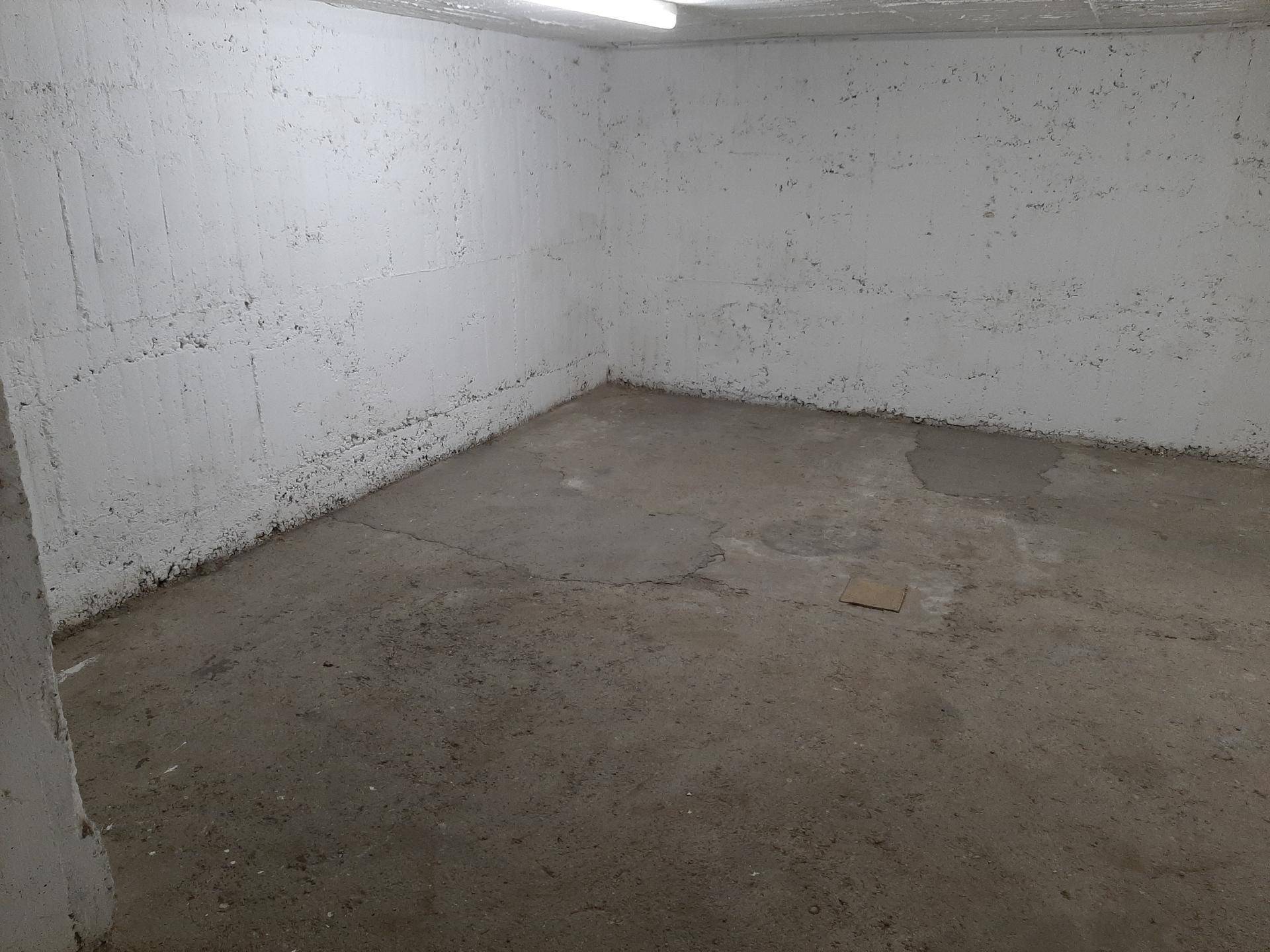 Leerer Lagerraum mit rauen, weiß gestrichenen Wänden und einem robusten Betonboden, funktional und geräumig.