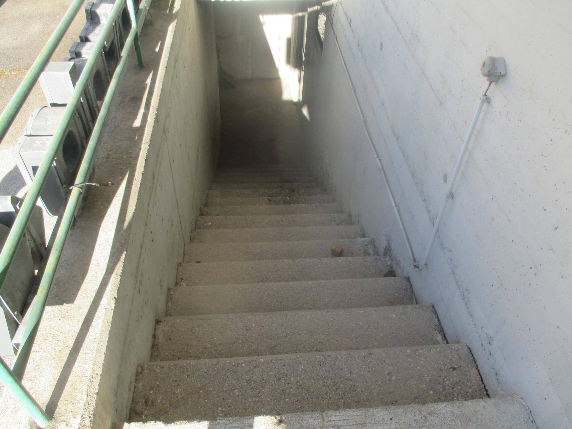 Betontreppe führt hinunter zu einem Untergeschoss oder einer Tiefgarage, ausgestattet mit einem stabilen Metallgeländer.