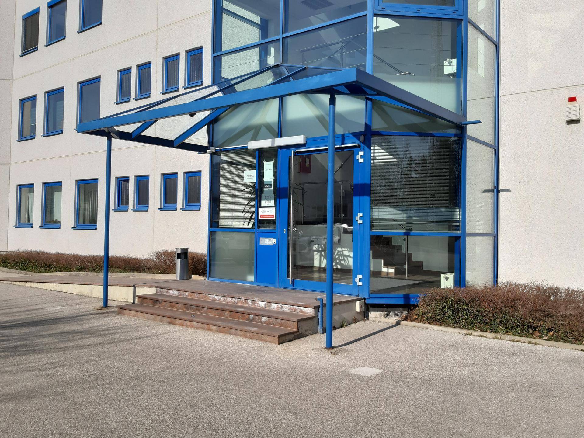 Eingangsbereich des Gebäudes mit blauer Glasüberdachung und automatischen Türen.