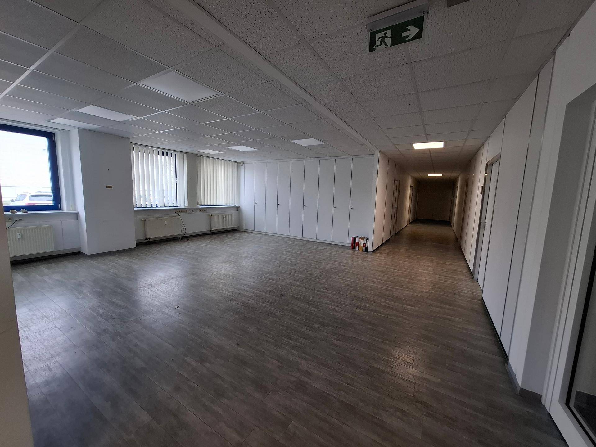 Großzügiger offener Büroraum mit Laminatboden, Einbauschränken und Blick in den Flur.