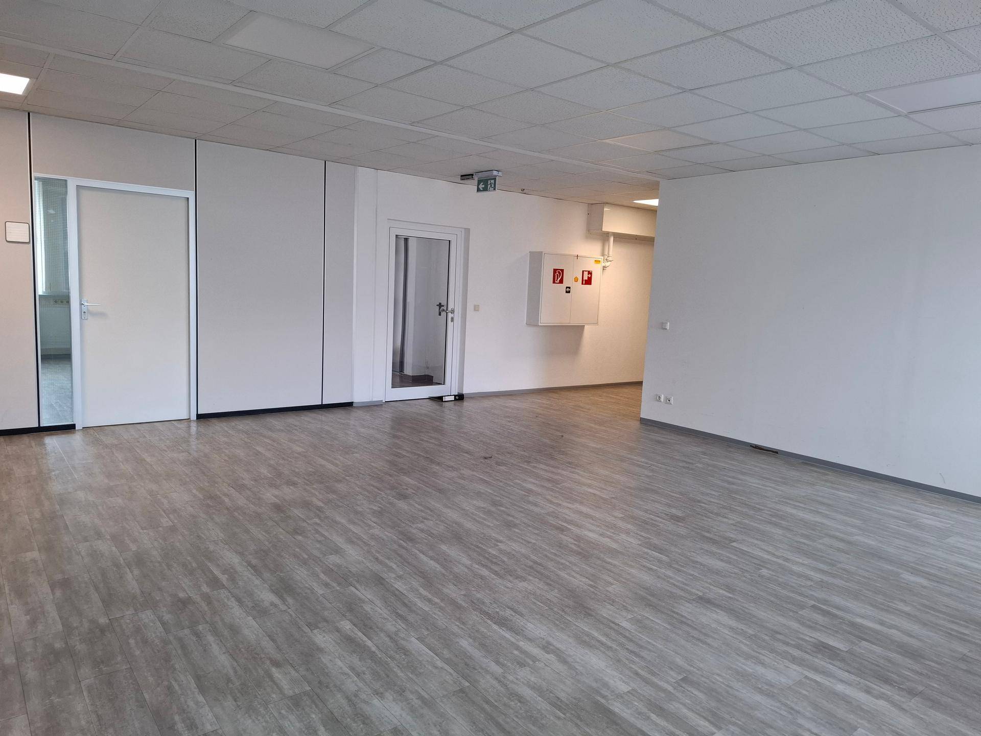 Offener Bürobereich mit Laminatboden, weißen Wänden und Türen zu weiteren Räumen.