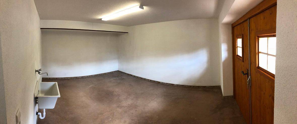 Großer Hauswirtschaftsraum mit Waschbecken, robustem Boden und Zugang nach draußen.