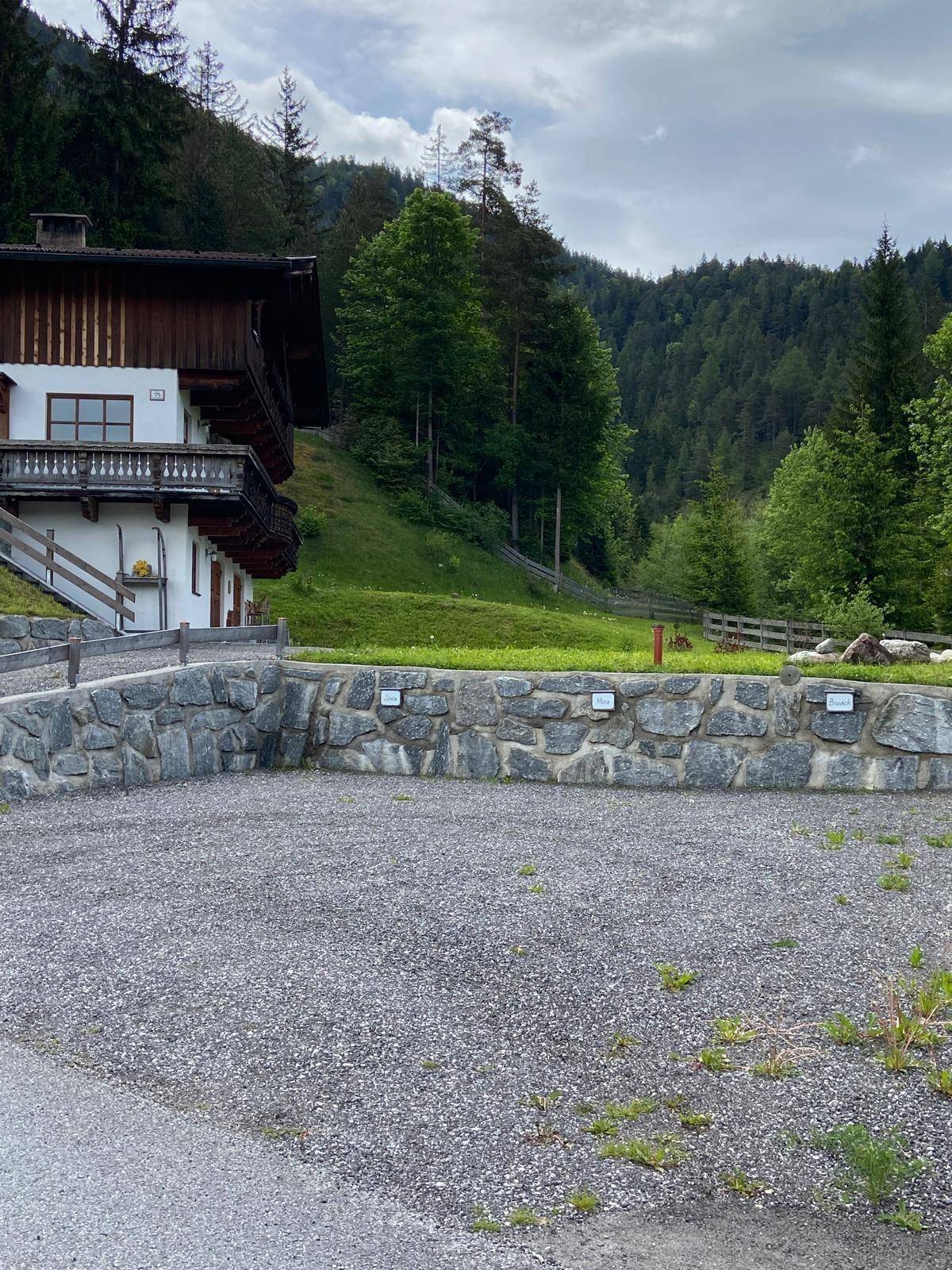 Großer Schotterparkplatz vor dem Haus mit einer Natursteinmauer und grüner Umgebung.