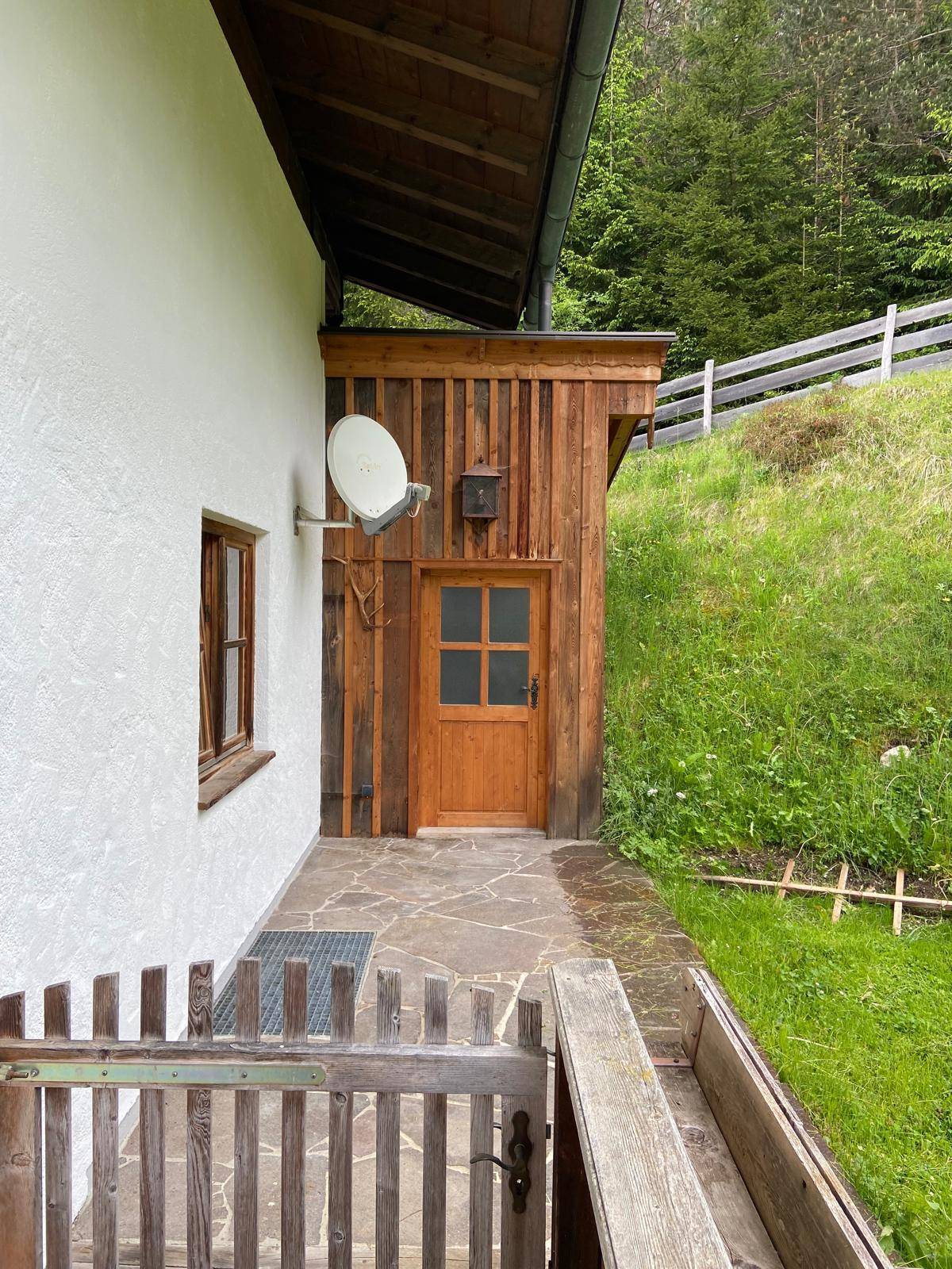 Seitlicher Eingangsbereich des Hauses mit Holztür, Satellitenschüssel und Steinfliesen.