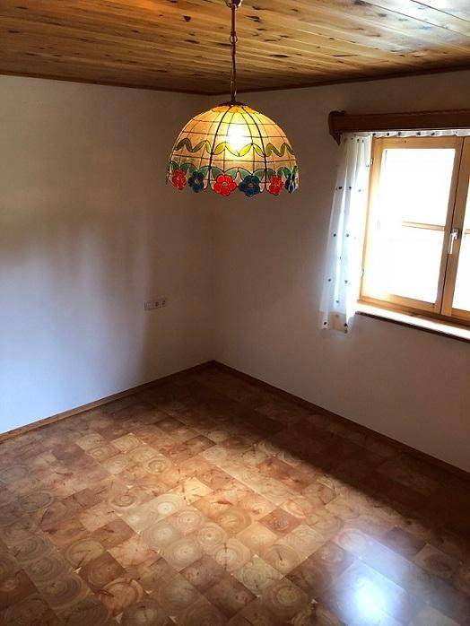 Helles Schlafzimmer mit Holzboden, Holzbalkendecke und einem Fenster mit Vorhängen.