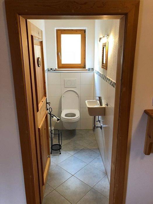 Kleines Gäste-WC mit Toilette, Handwaschbecken und Fenster für natürliche Belüftung.