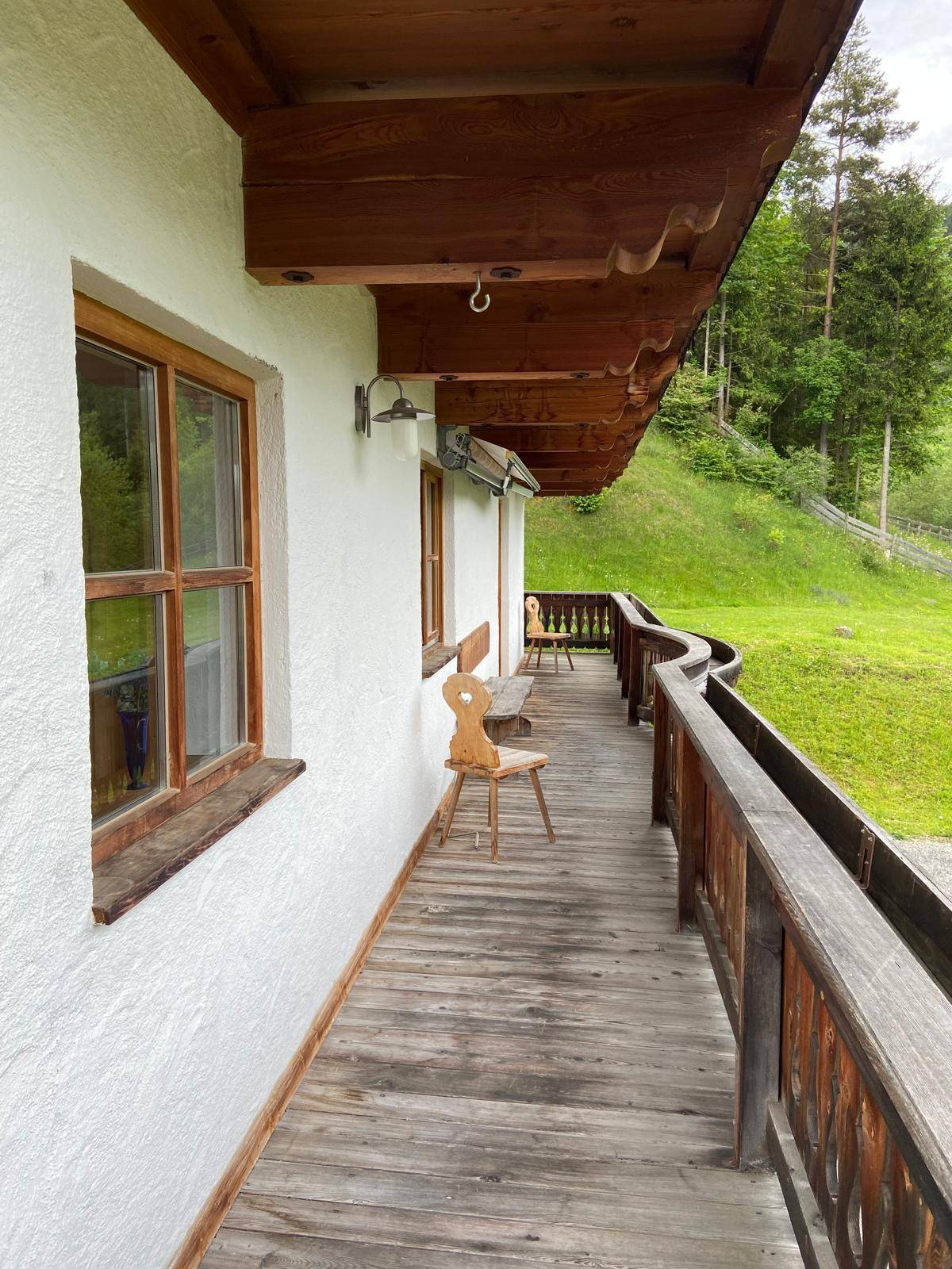 Langer Holzbalkon mit traditionellem Geländer und malerischem Blick auf die umliegenden Berge.