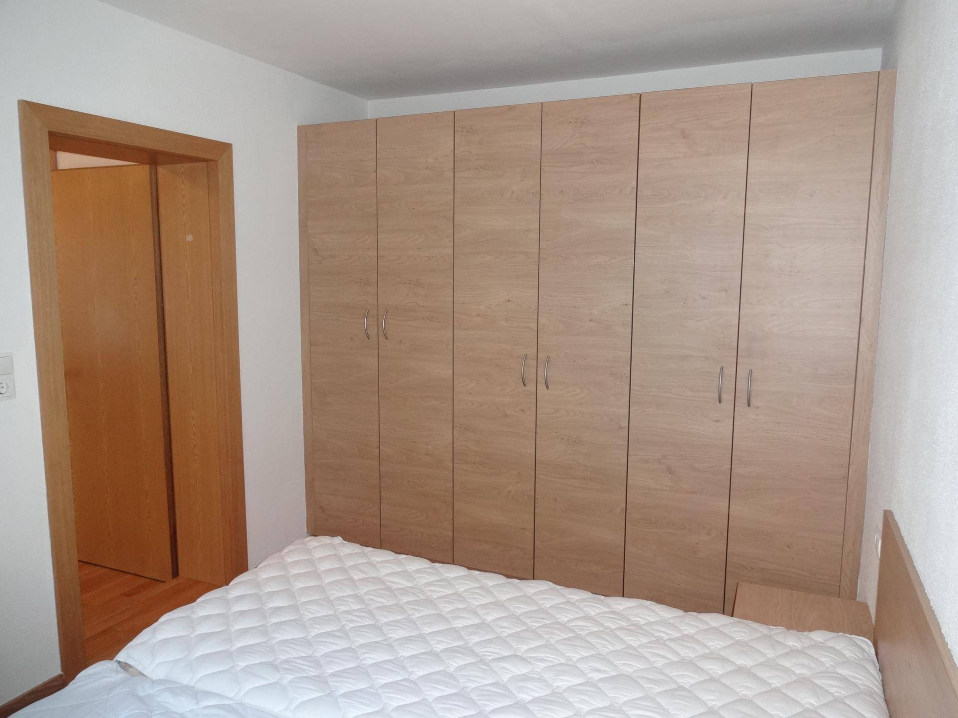 Schlafzimmer mit großem Einbauschrank und Doppelbett, in hellem Holz gehalten.