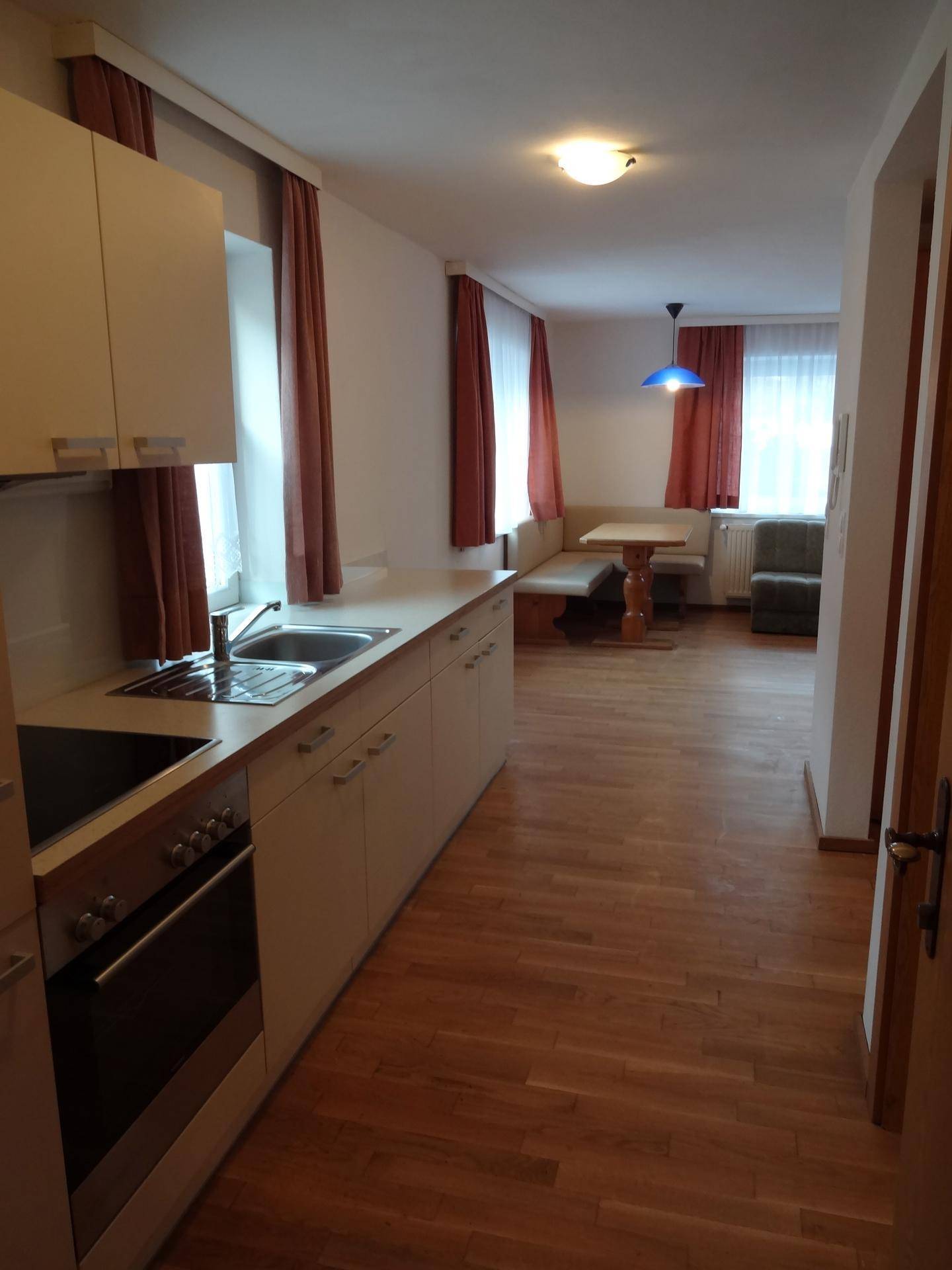 Offener Wohnbereich mit Küchenzeile, Essbereich und Sofa, alles auf Holzboden.