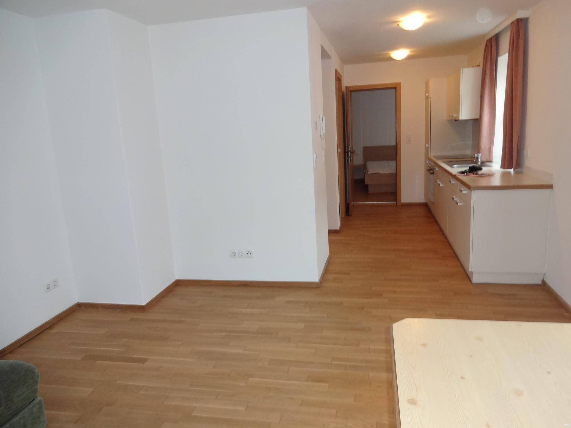 Heller Bereich mit Holzboden, der zu einer Küchenzeile und einem weiteren Zimmer führt.