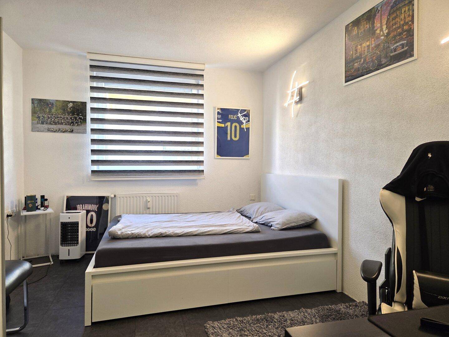 Jugendzimmer mit Bett, Schreibtisch und Fenster mit Jalousien.