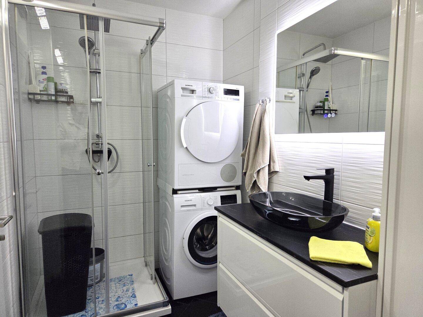 Modernes Badezimmer mit ebenerdiger Dusche, Waschmaschine und Trockner.