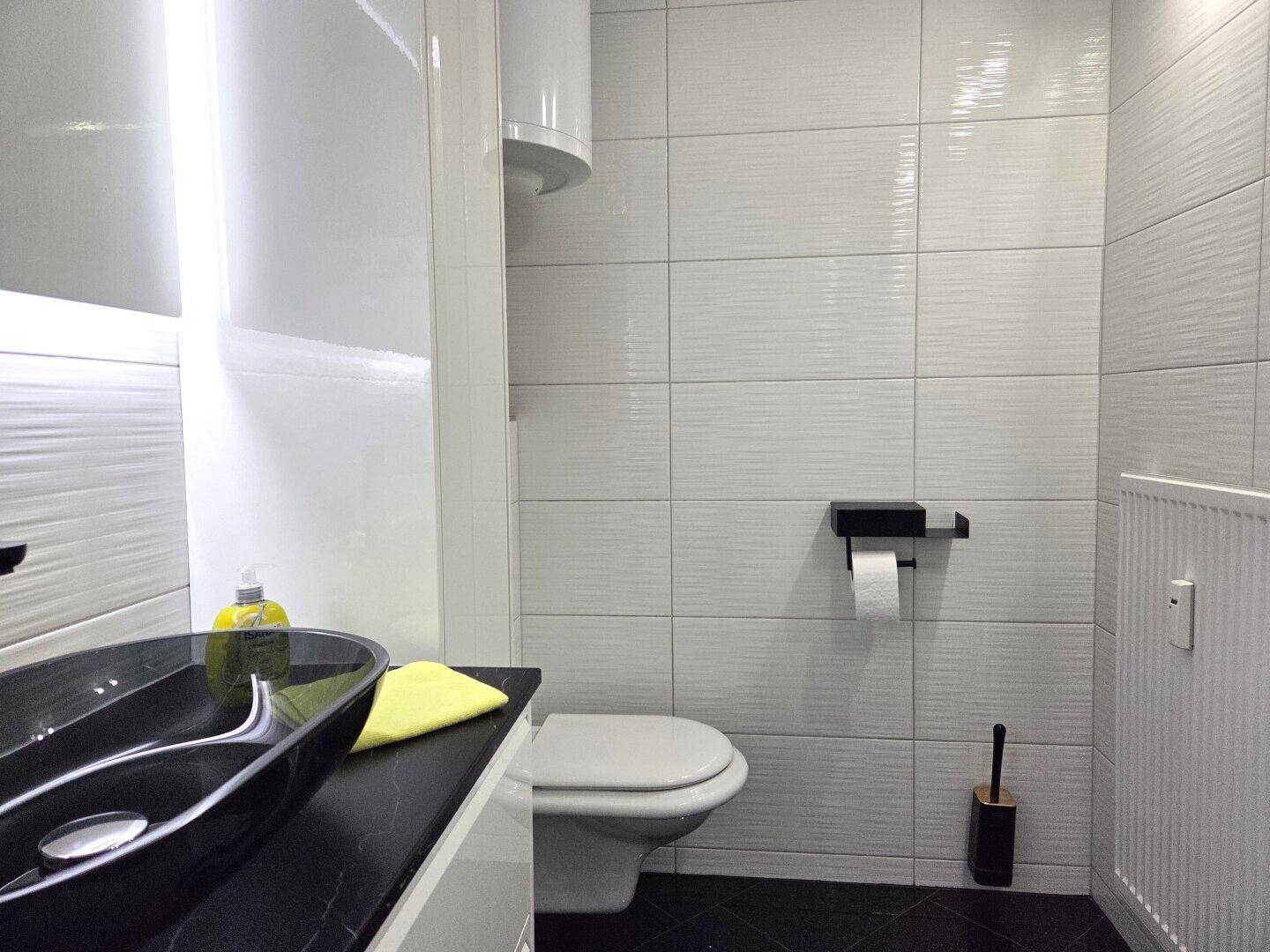 Helles Badezimmer mit modernem Waschtisch, wandhängendem WC und weißen Fliesen.