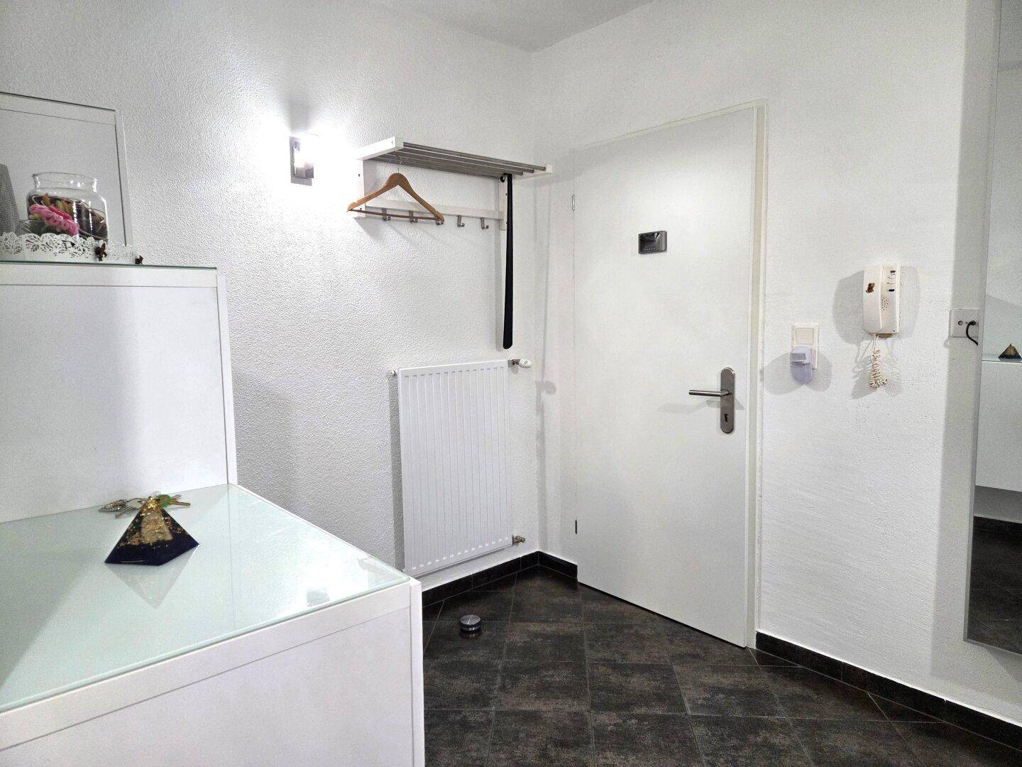 Heller Eingangsbereich mit Garderobe, Heizkörper und dunklem Fliesenboden.