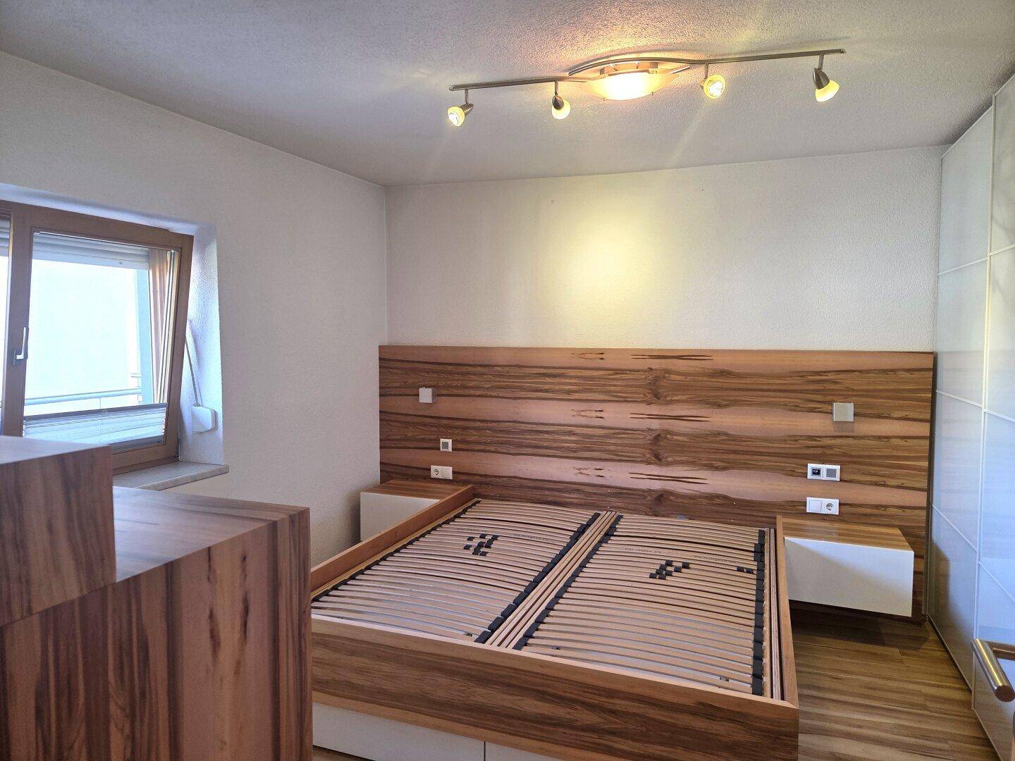 Schlafzimmer mit Holzbettrahmen, passendem Kopfteil und einem großen weißen Einbauschrank.
