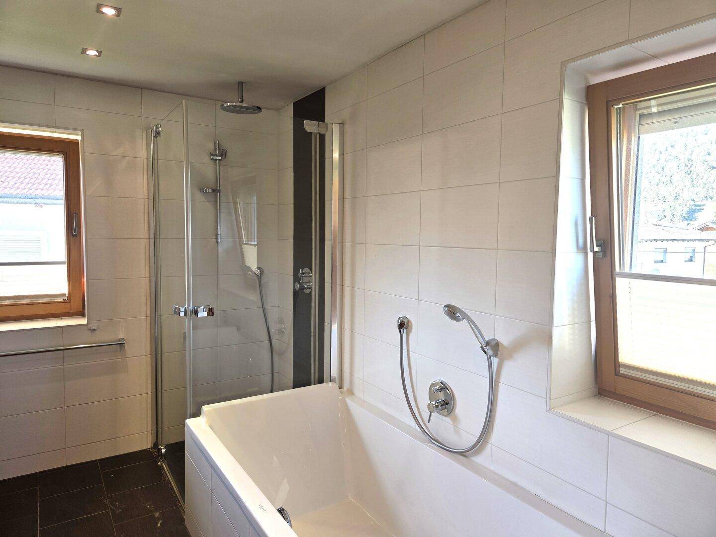 Modernes Badezimmer mit Badewanne, begehbarer Dusche und zwei Fenstern für Tageslicht.