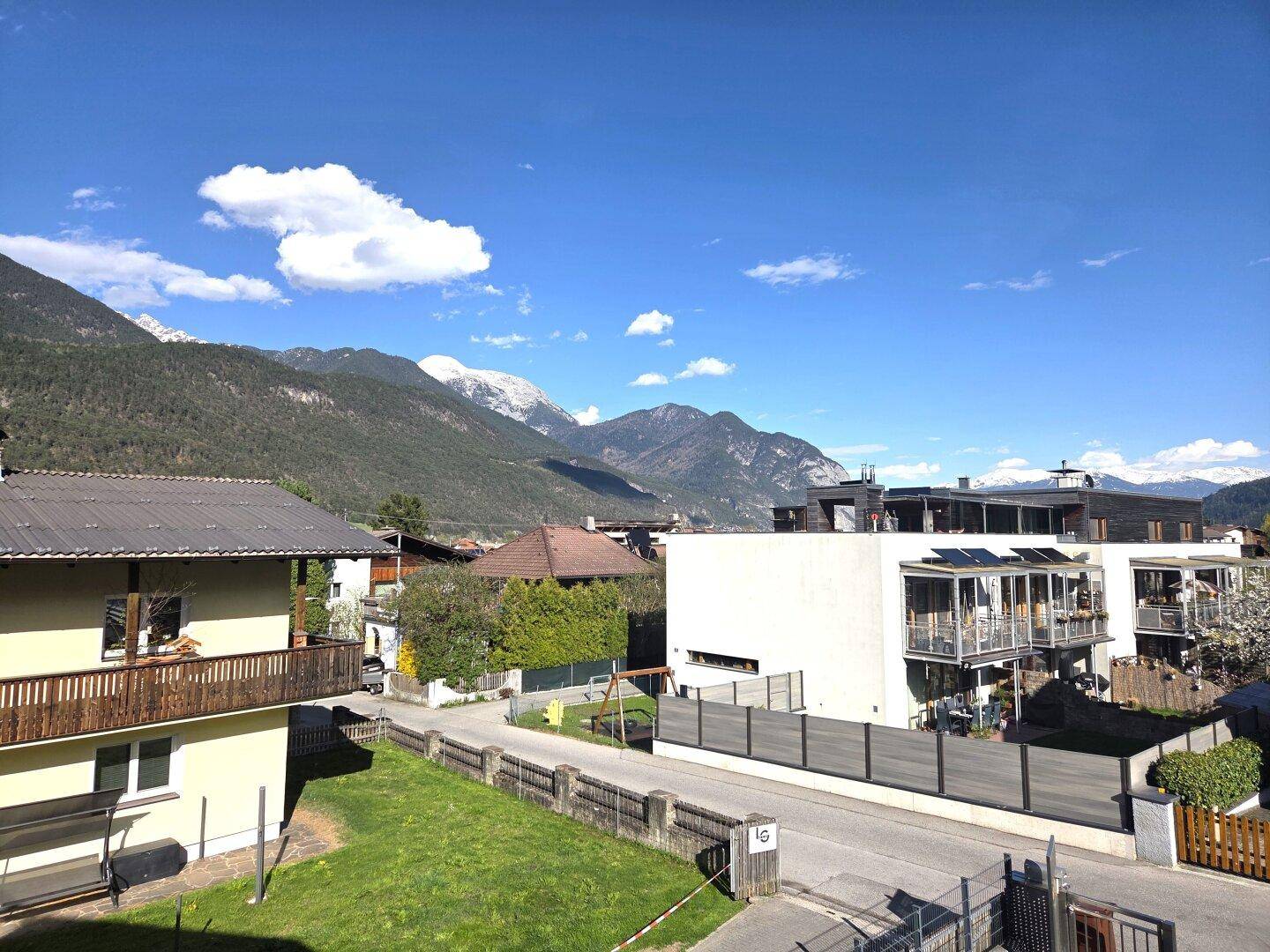 Panoramablick auf die umliegende Wohngegend mit grünen Gärten und schneebedeckten Bergen.
