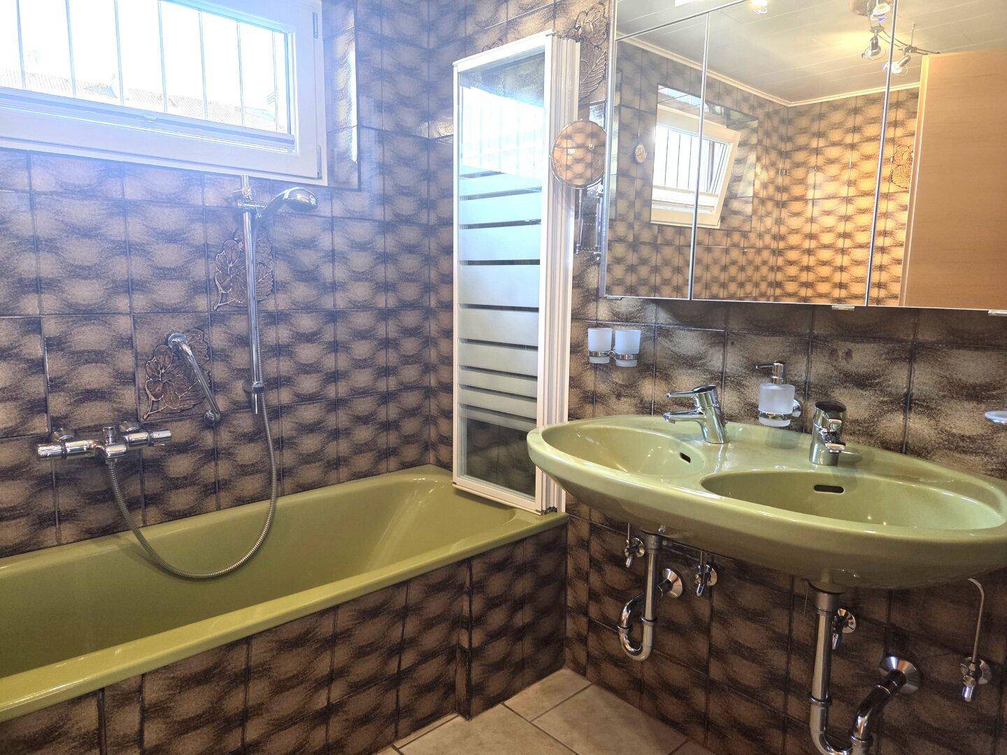 Badezimmer im Stil der 80er Jahre mit grüner Badewanne und gemusterten Fliesen.