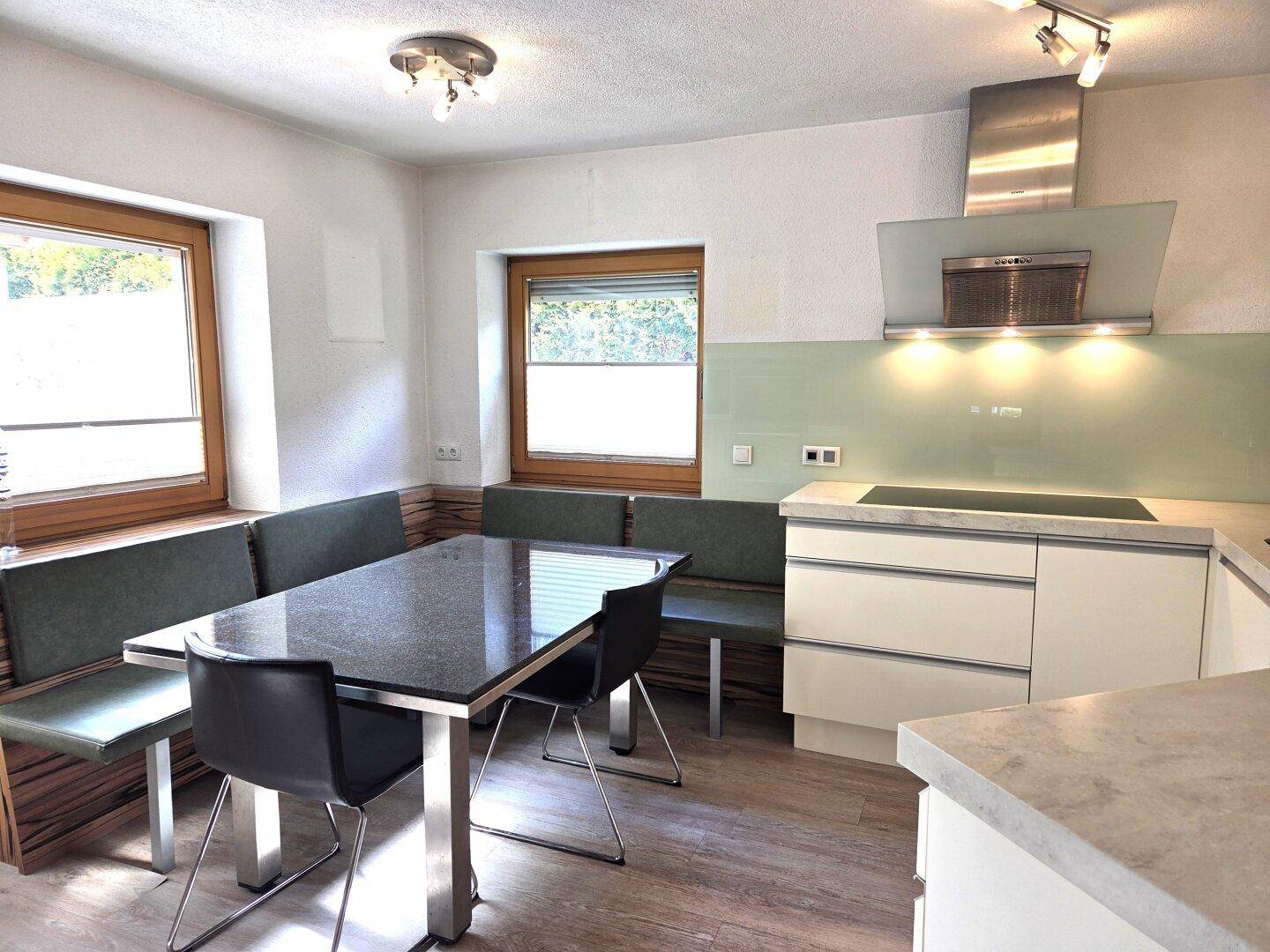 Moderne Küche mit Essbereich, weißen Schränken, Induktionskochfeld und hellgrüner Rückwand.