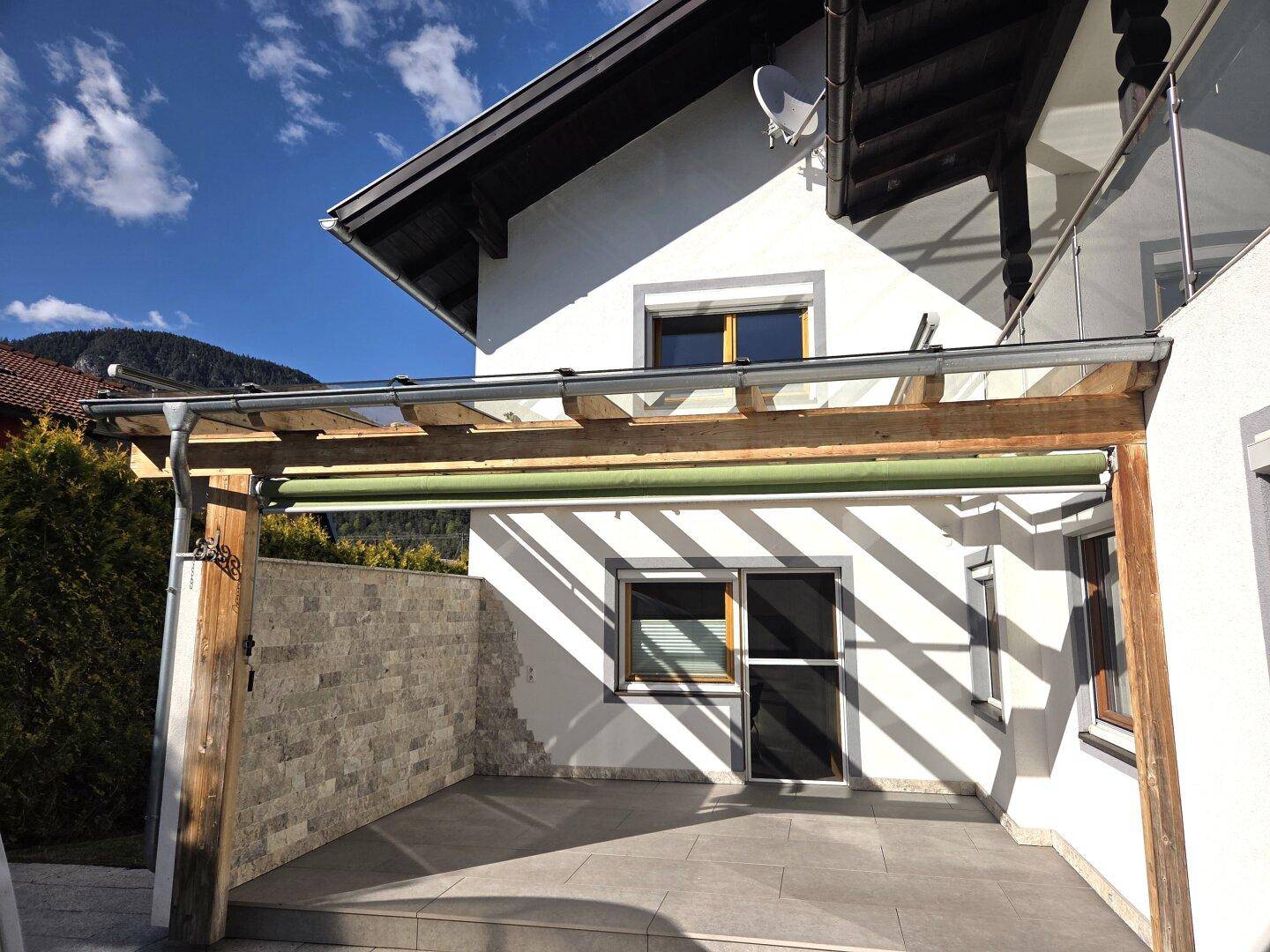 Überdachte Terrasse mit Holzbalken und Steinwand, ideal für entspannte Stunden im Freien.