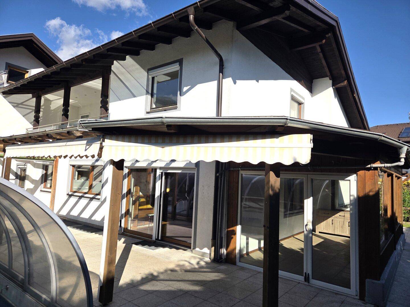 Seitenansicht des Hauses mit überdachter Terrasse und großen Glasfronten, die viel Licht ins Innere lassen.