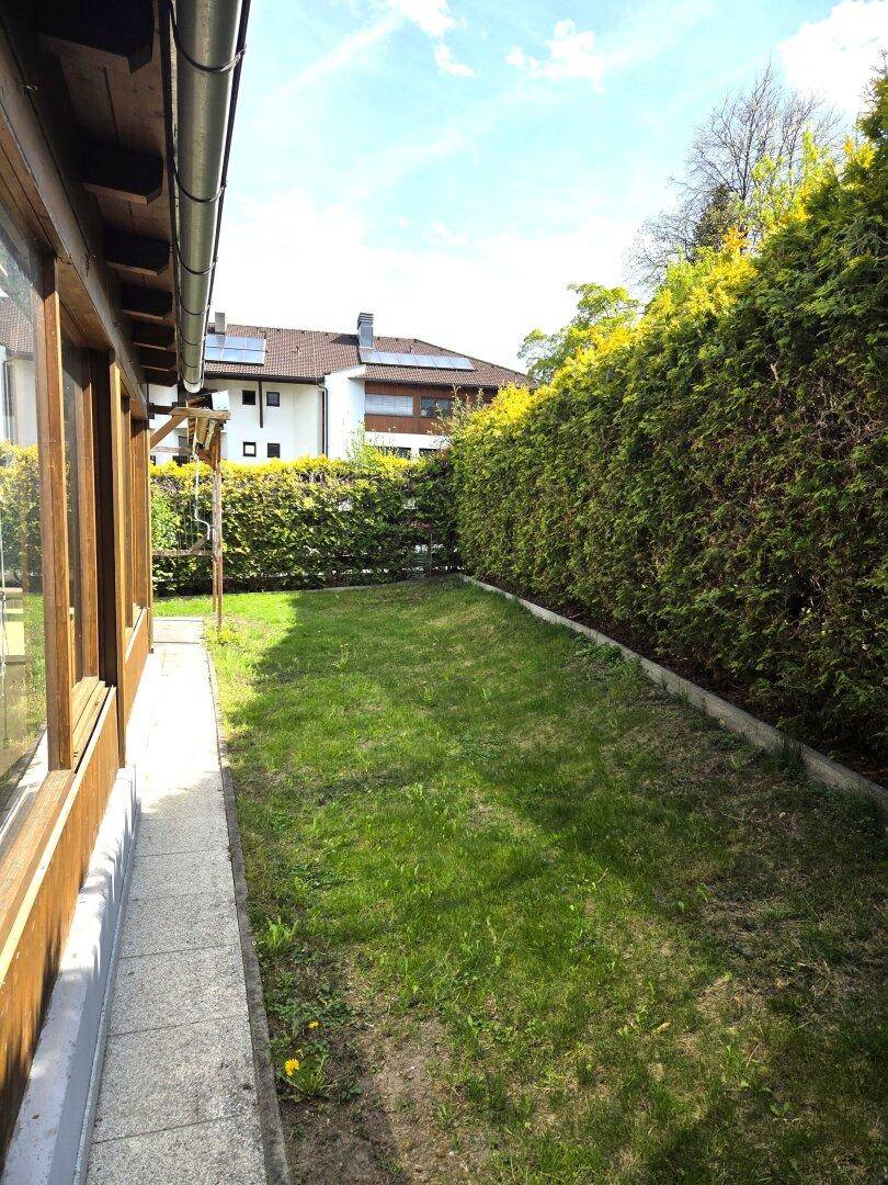 Schmaler Gartenstreifen entlang des Hauses, umgeben von einer hohen Hecke für Privatsphäre.
