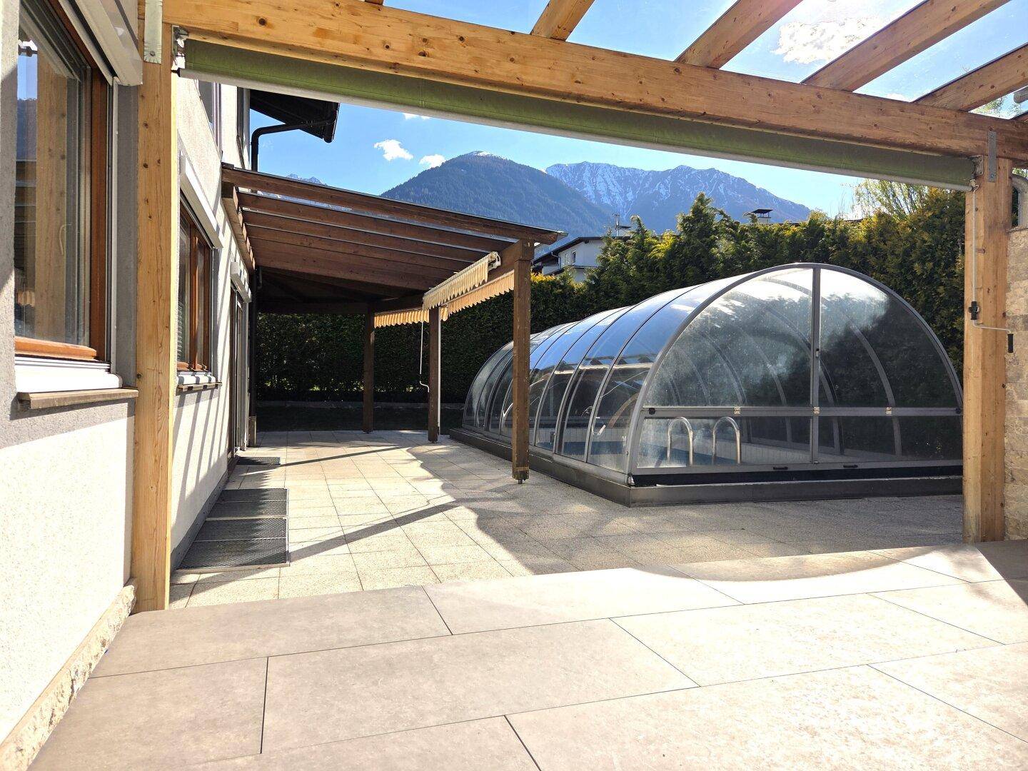 Große gepflasterte Terrasse mit überdachtem Pool und Blick auf die umliegenden Berge.
