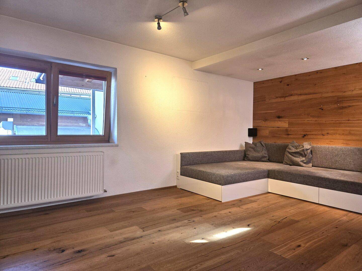 Helles Wohnzimmer mit Holzboden, moderner Eckcouch und einer Holzwand als Akzent.