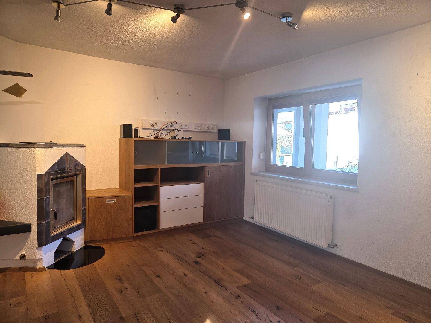 Gemütliches Wohnzimmer mit Holzboden, Kachelofen und einem Fenster für natürliches Licht.