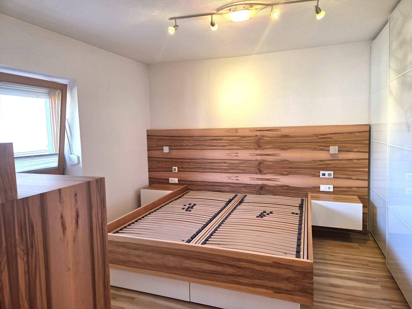 Schlafzimmer mit modernem Holzbett, passendem Kopfteil und weißem Kleiderschrank.