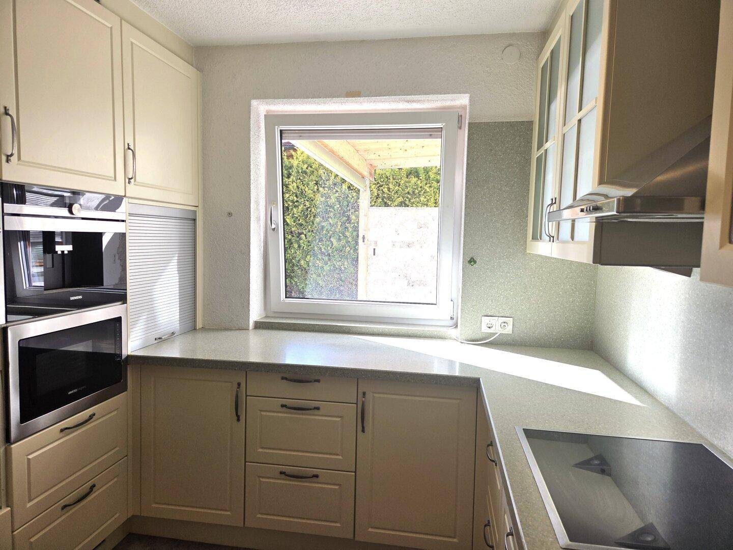 Helle Küche mit cremefarbenen Schränken, integriertem Backofen und Fenster.