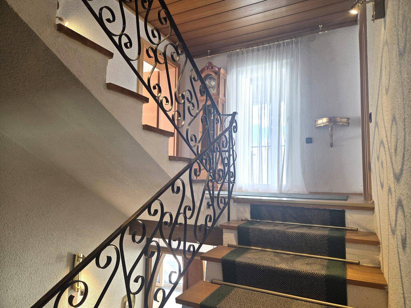 Treppenhaus mit Holzstufen, Teppichläufer und schmiedeeisernem Geländer.