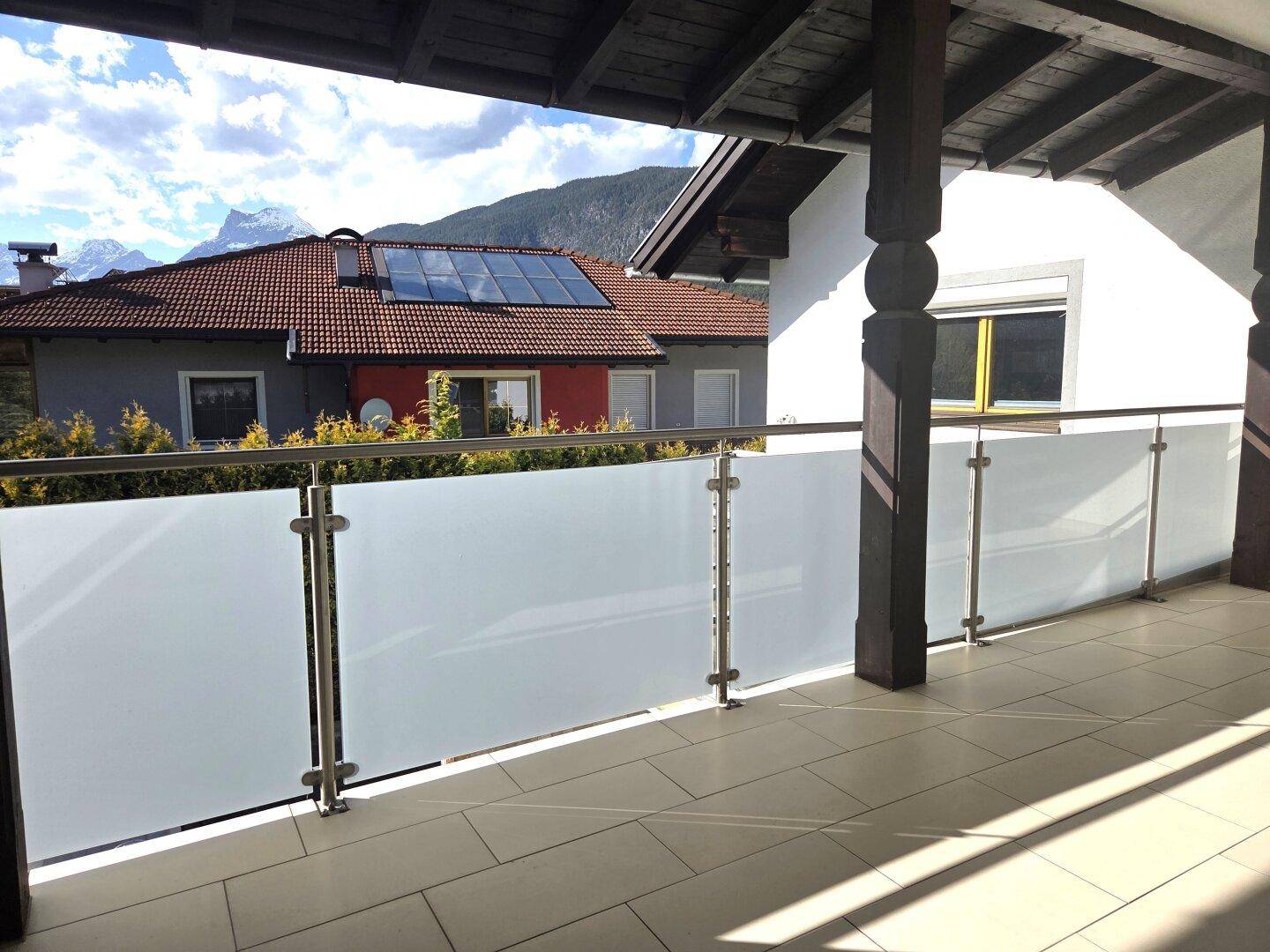 Überdachter Balkon mit Milchglasgeländer und weitem Blick auf die Berge.
