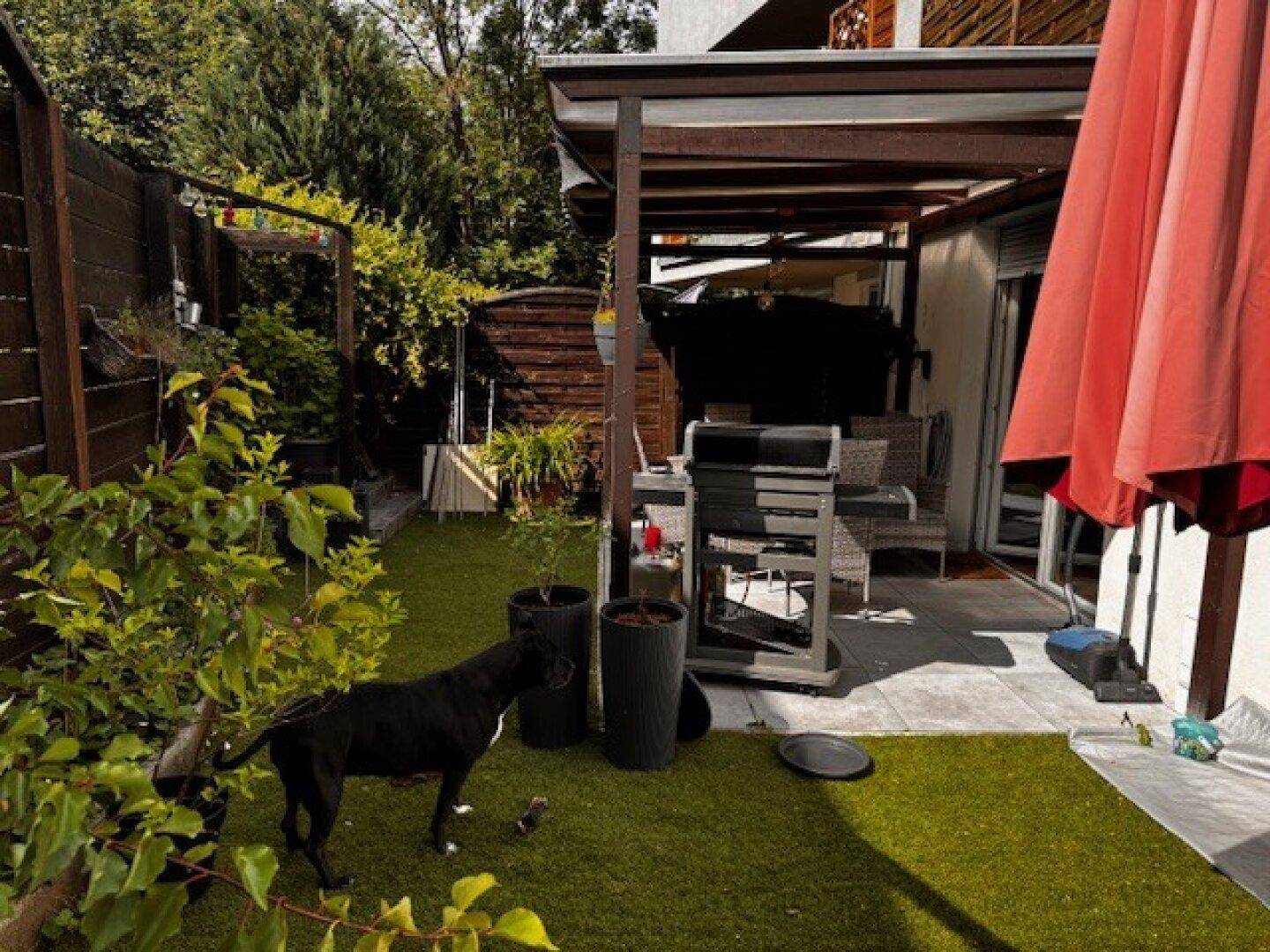 Sonniger Außenbereich mit überdachter Terrasse, Grill und Kunstrasen, ideal für Entspannung.