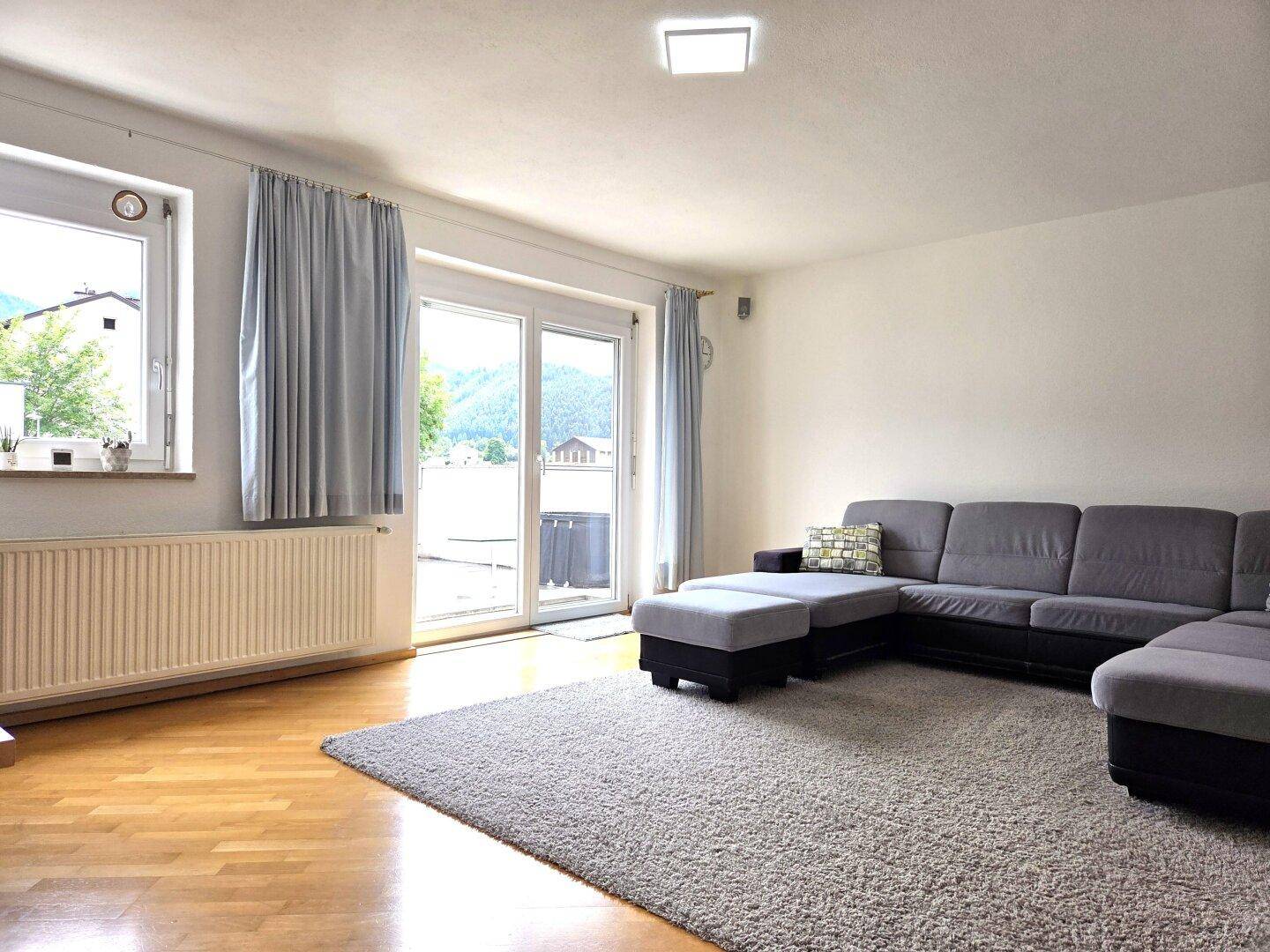 Helles Wohnzimmer mit großem Ecksofa, Holzboden und Zugang zu einem Außenbereich mit Bergblick.