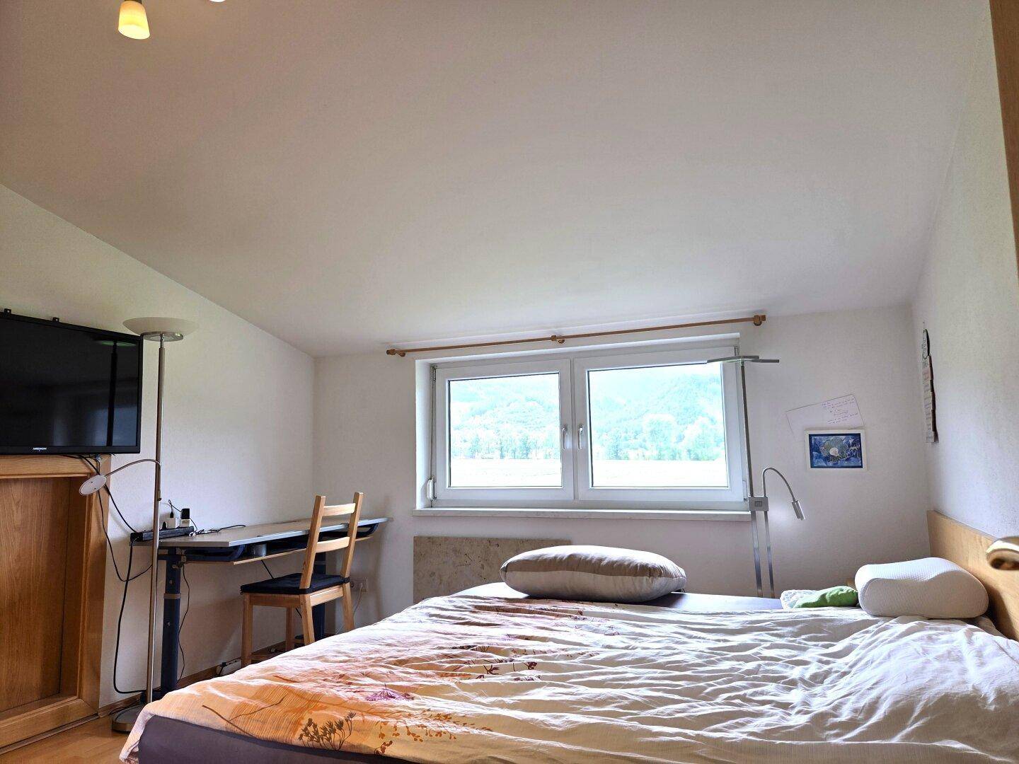 Schlafzimmer mit Doppelbett, Schreibtisch und Fenster, das einen weiten Blick auf die grüne Landschaft bietet.