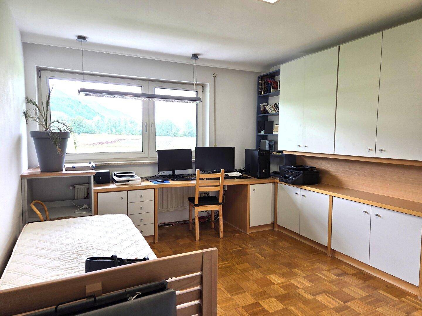Helles Arbeitszimmer mit großem Schreibtisch, Einbauschränken und Blick ins Grüne durch das Fenster.